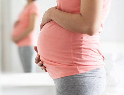 pregnant woman holding her belly and  looking in the mirror
